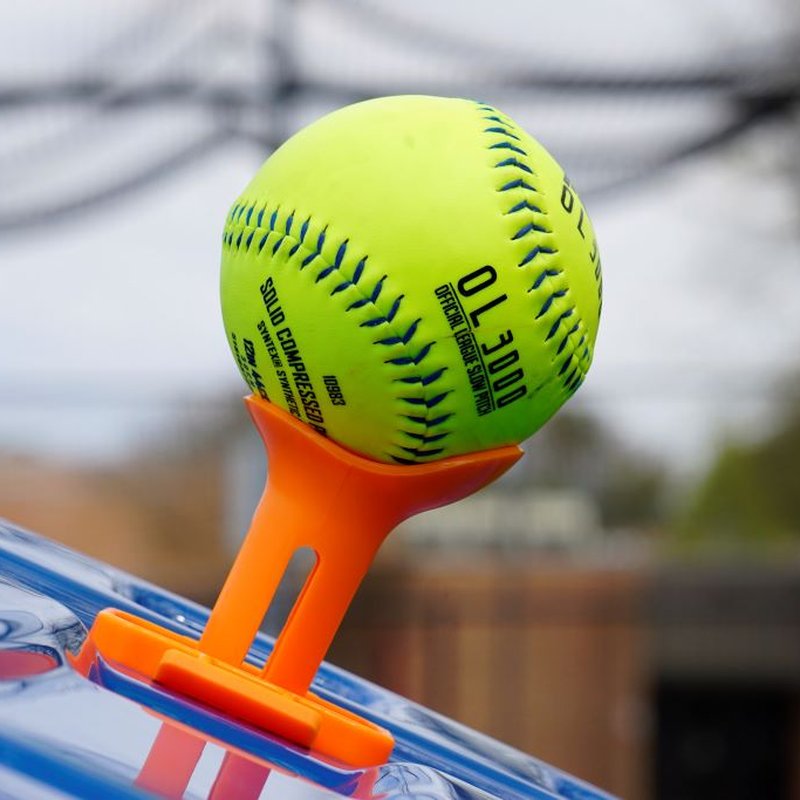A softball resting on the tee topper with netting behind.