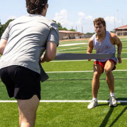 Two athletes on a field working a partner resistance drill with a long fabric band