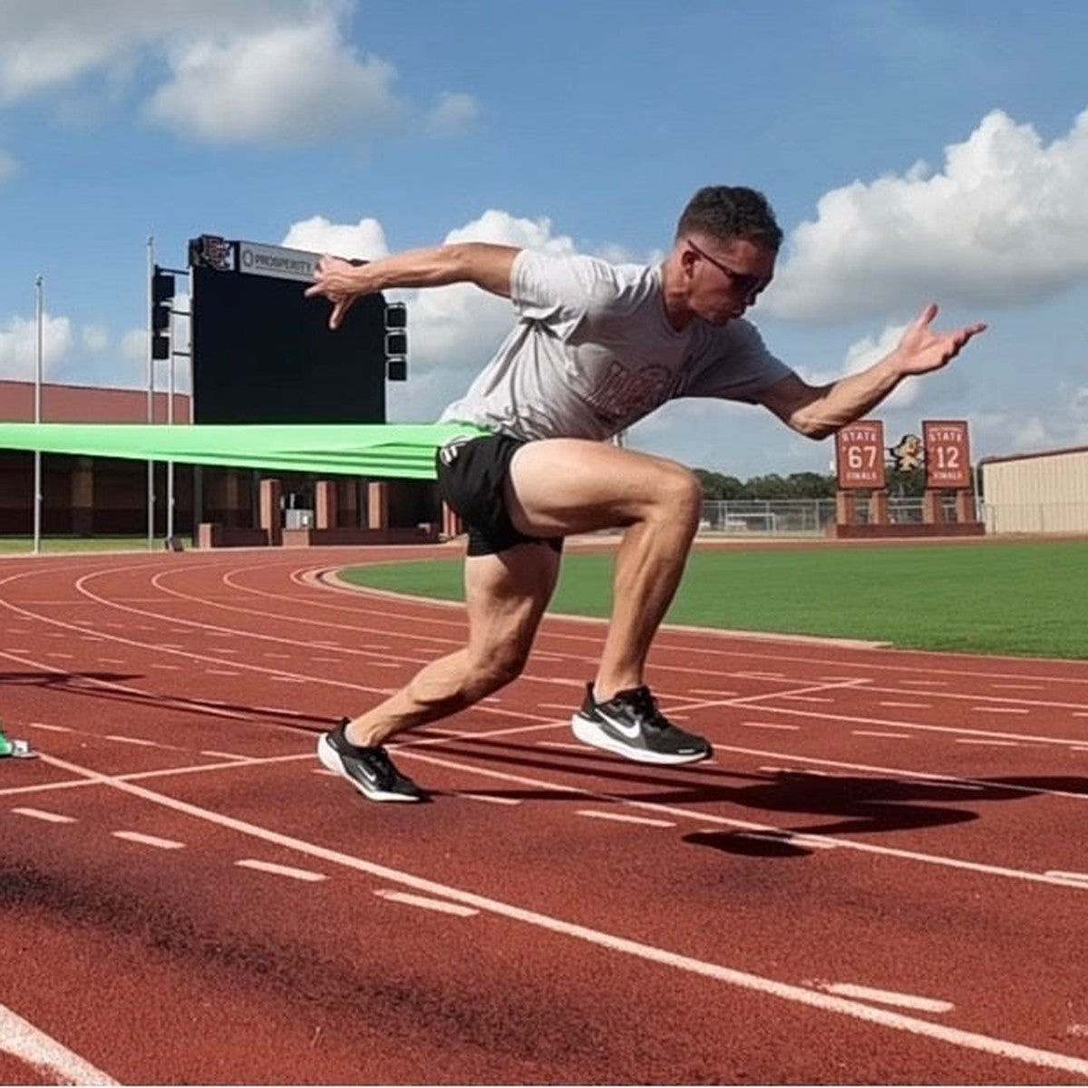 Partner holding a long green resistance band as an athlete drives out of a start on a track