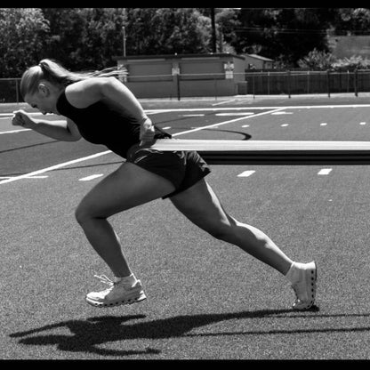 Athlete leaning into an explosive first step against a resistance band around her waist