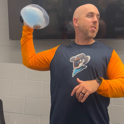 Baseball coach in uniform taking the water-filled football through a slow overhead throwing motion