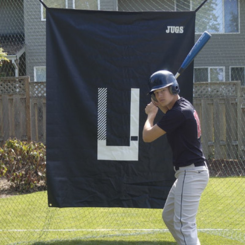 A baseball hitter standing in front of the JUGS Backdrop and Pitcher's Trainer hung in a backyard.