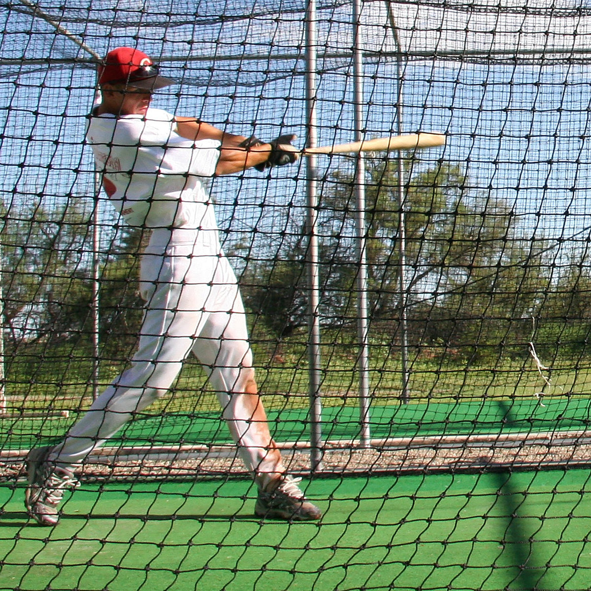 A hitter swinging inside a black JUGS twisted knotted polyethylene batting cage net on an outdoor field.