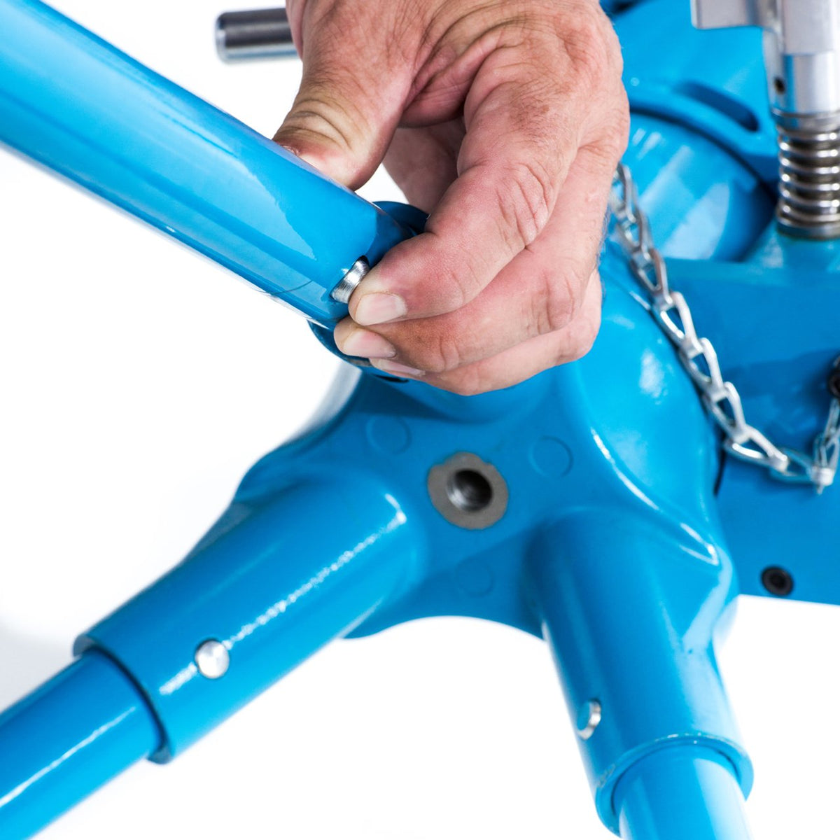 Close-up of a hand fitting a tripod leg into the light blue cast base of a JUGS BP3 pitching machine.