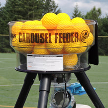 The JUGS Carousel automatic ball feeder with a clear acrylic hopper full of yellow practice balls, mounted on its black tripod frame.