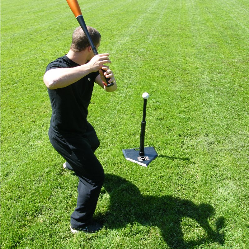 A baseball hitter loading to swing at a ball on the JUGS Hit Like a Pro Hitting Tee on a grass field.
