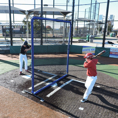 Two baseball players hitting near the JUGS Protector Blue Series 8-Foot Fungo Screen in a batting area.