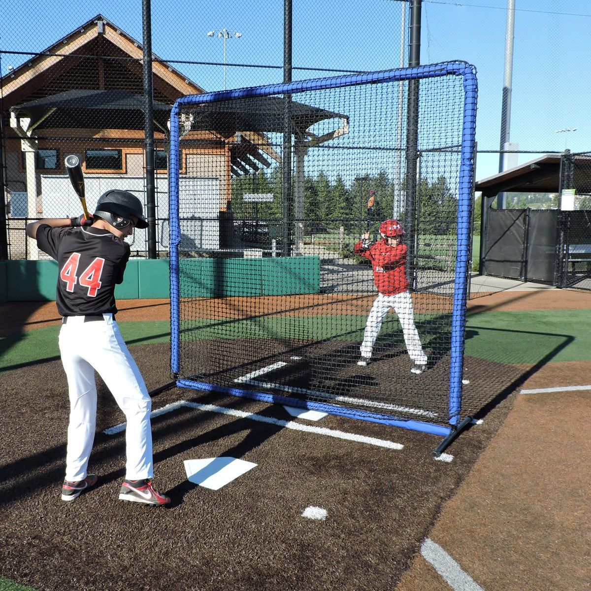 Baseball players working near home plate with the JUGS Protector Blue Series 8-Foot Fungo Screen.