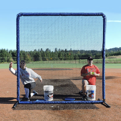 Two coaches seated behind the JUGS Protector Blue Series 8-Foot Fungo Screen on a dirt infield.