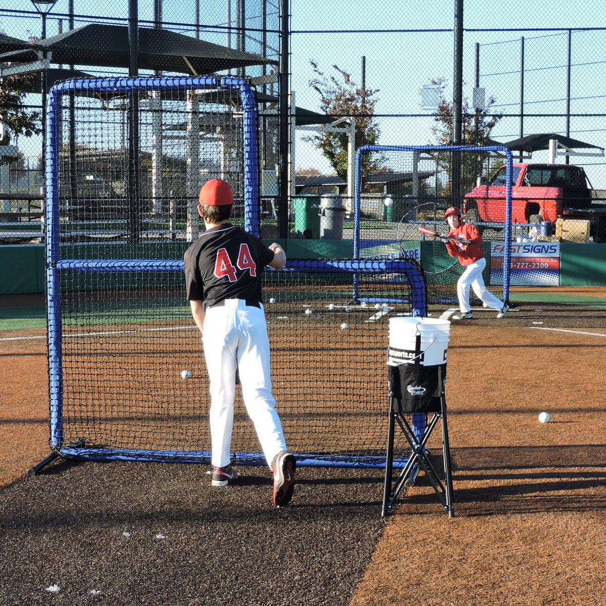 A youth pitcher throwing batting practice from behind the JUGS Protector Blue Series L-Shaped Pitchers Screen.