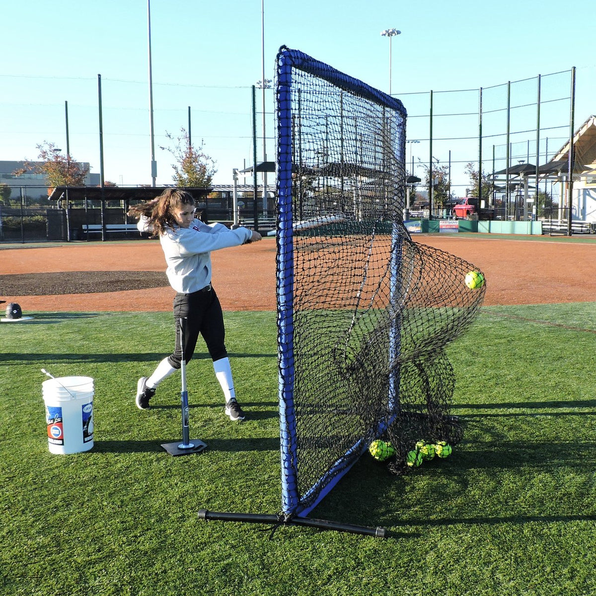 A softball player hitting off a tee into the JUGS Protector Blue Series Square Screen with Sock-Net on turf.