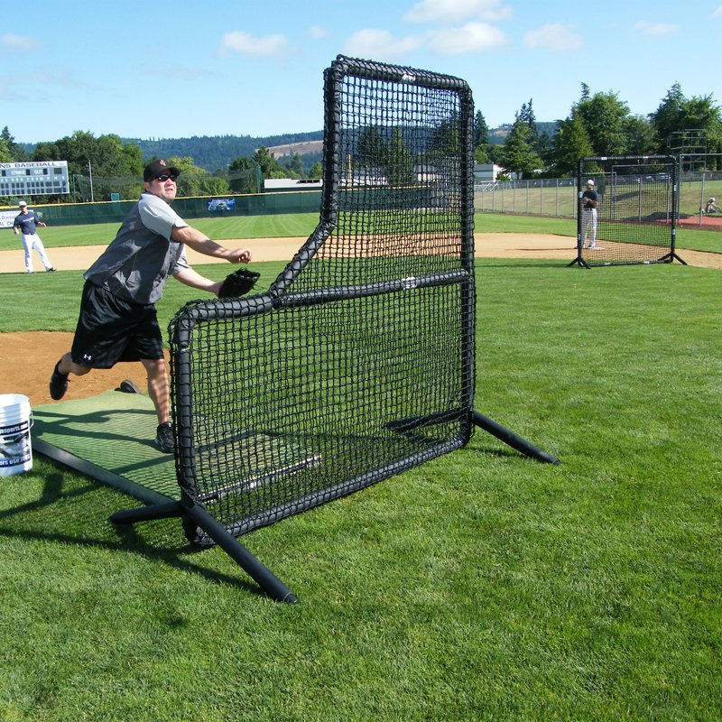 A coach throwing batting practice from behind the JUGS Protector Series L-Shaped Screen on a field.