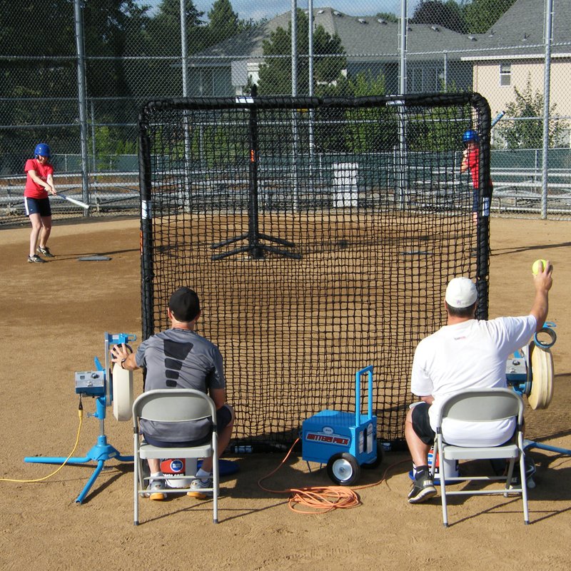 Two coaches feeding JUGS pitching machines from behind the JUGS Protector Series Square Baseman Screen.