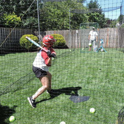 A young hitter in a batting helmet swinging at a pitch from a JUGS PS50 in a backyard batting cage.
