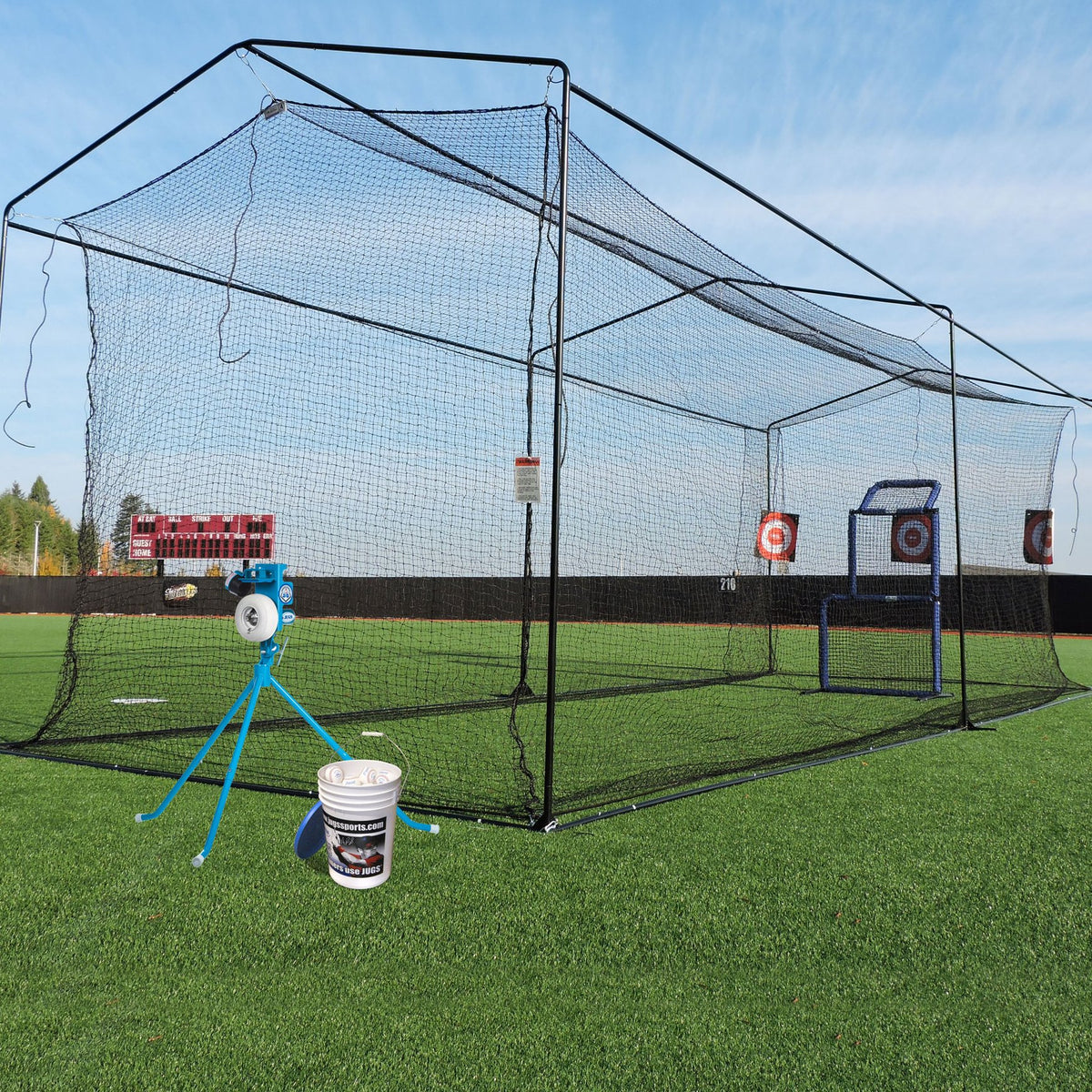 The JUGS Short-Toss Package set up on a grass field: free-standing short-toss cage, PS50 pitching machine, bucket of balls and target.