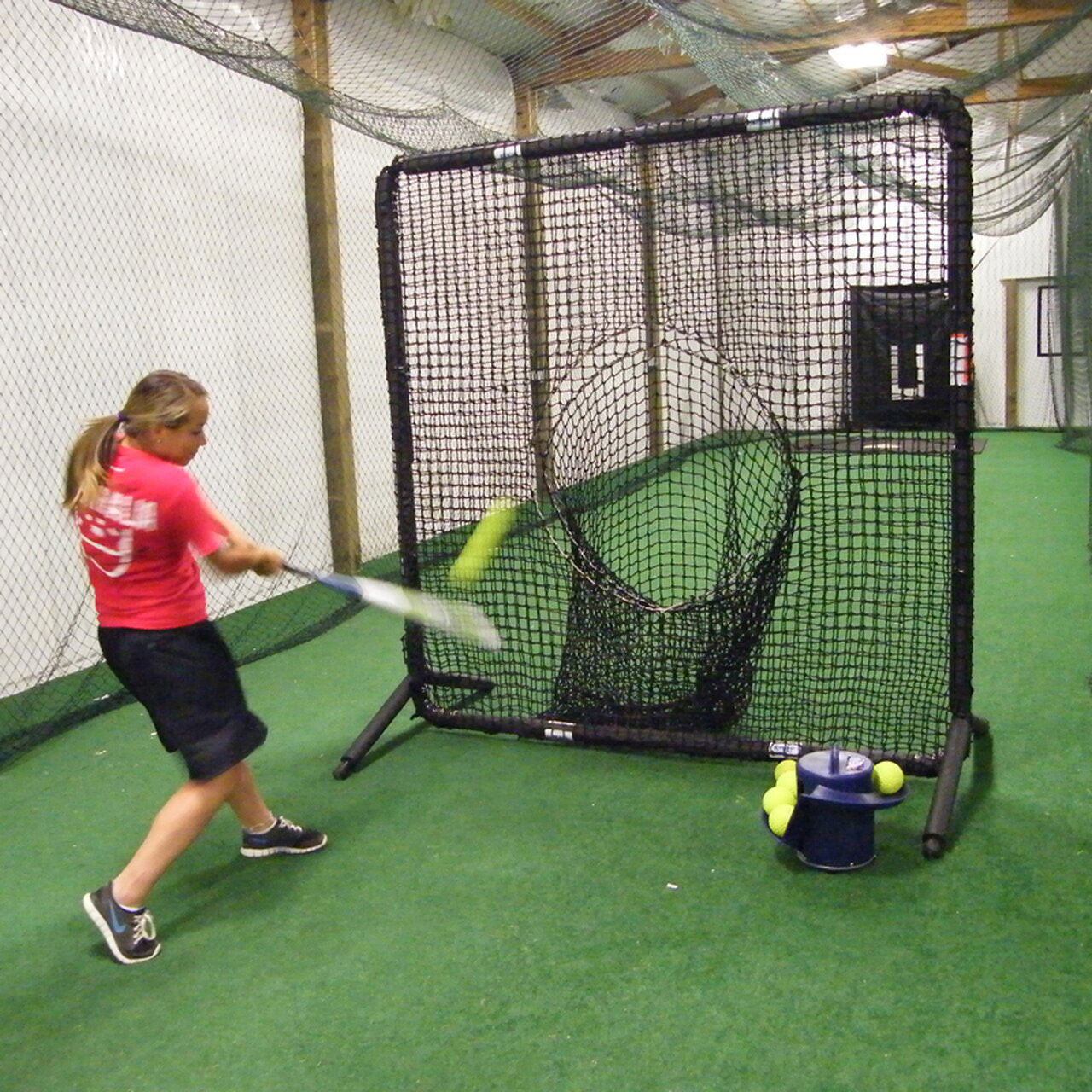 Softball player hitting soft tossed balls into a sock net inside a training facility