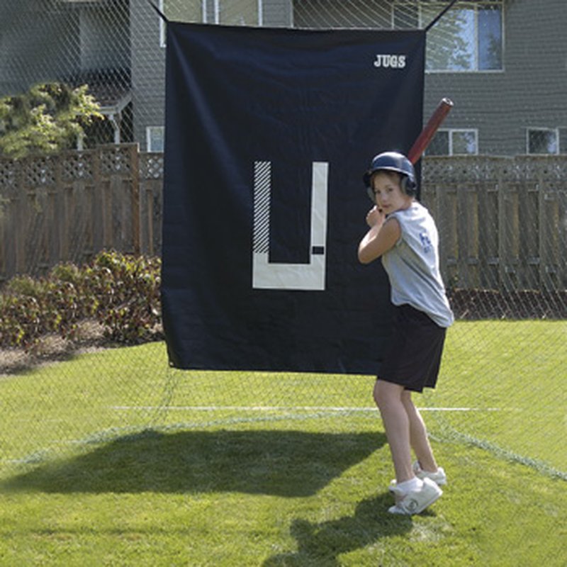 A softball hitter standing in front of the JUGS Backdrop and Pitcher's Trainer hung in a backyard.