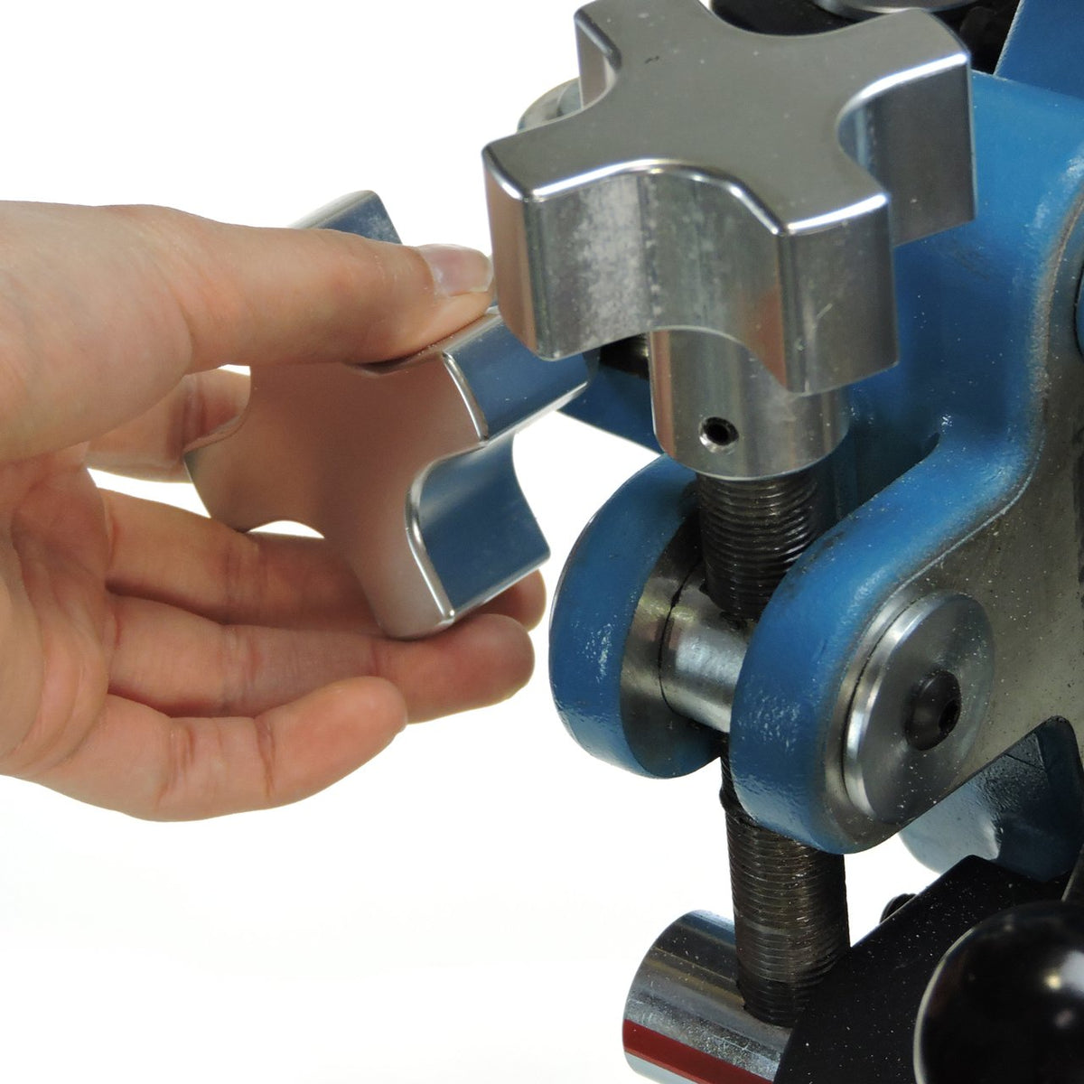 A hand turning the large star-shaped micro-adjustment knob on the head of a JUGS three-wheel softball machine, photographed on a white background.