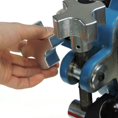 A hand turning the large star-shaped micro-adjustment knob on the head of a JUGS three-wheel softball machine, photographed on a white background.
