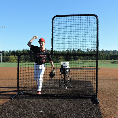 A youth pitcher throwing from behind the JUGS Standard L-Shaped Pitchers Screen on a dirt mound.