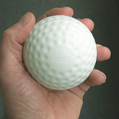 A hand holding a white dimpled practice baseball with JUGS embossed on it, against a dark background.