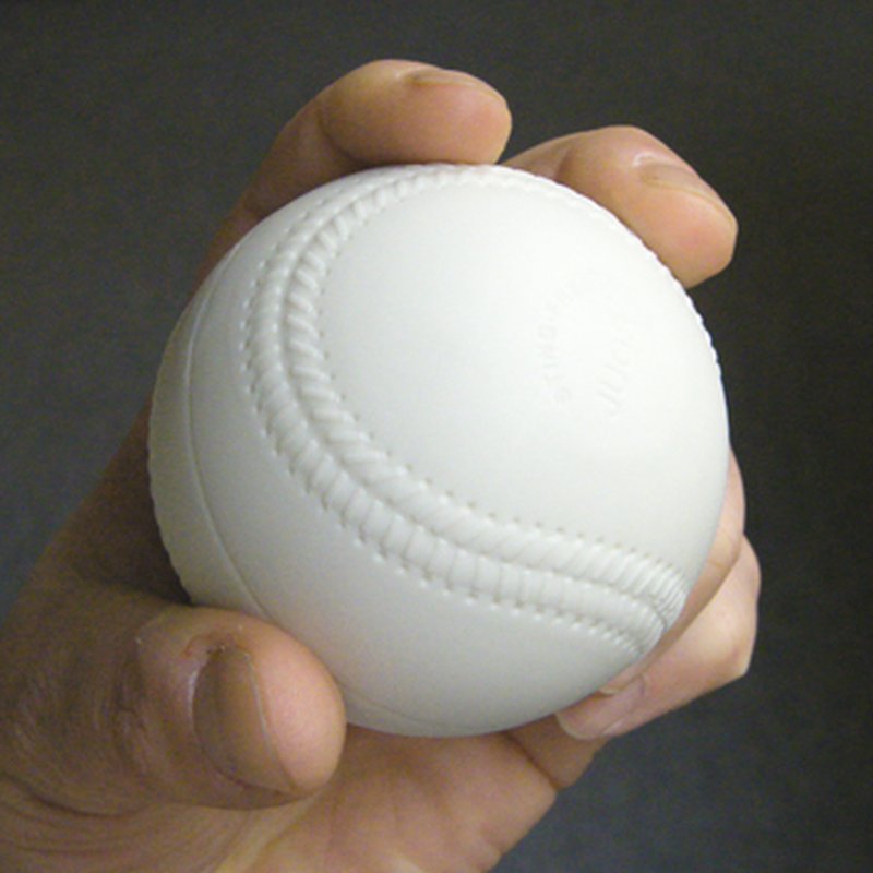 A hand gripping a white practice baseball with raised molded seams, against a dark background.
