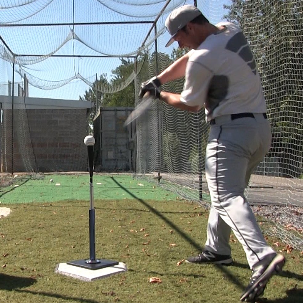 A baseball player hitting off the JUGS T inside a batting cage.