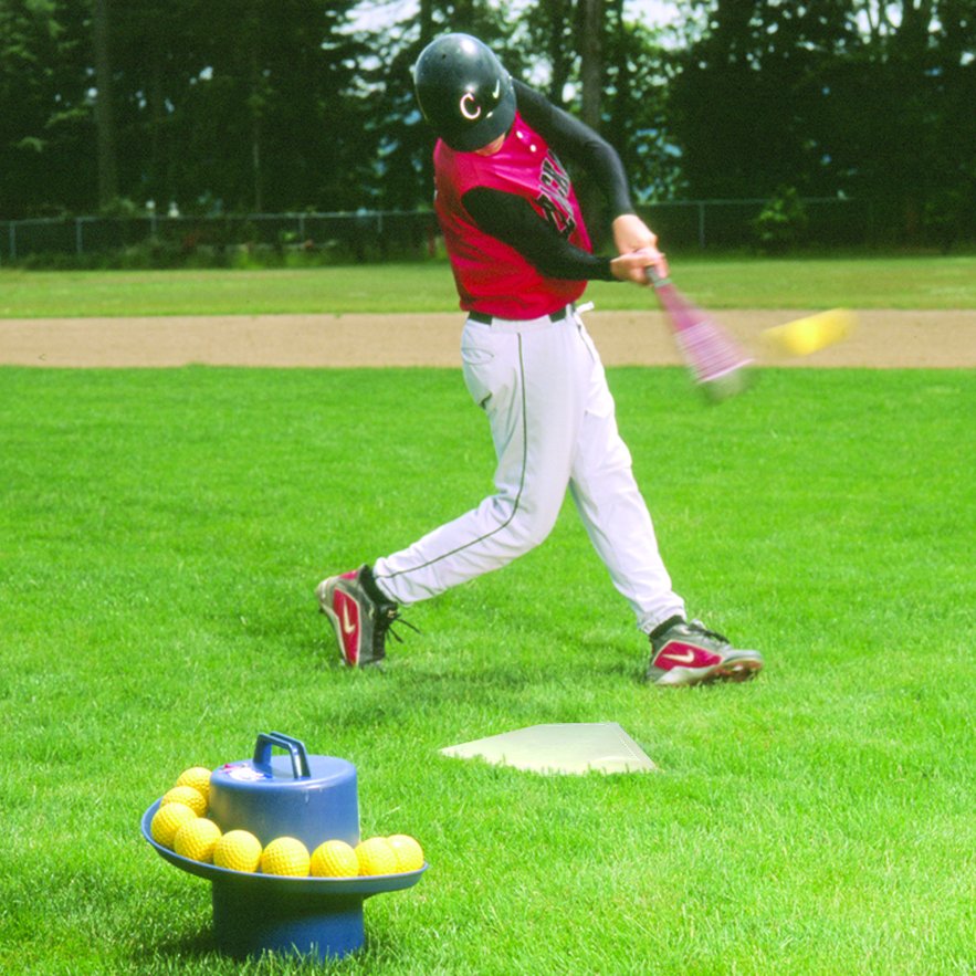 A baseball player swinging at a ball tossed by the JUGS Toss Machine on a grass field.