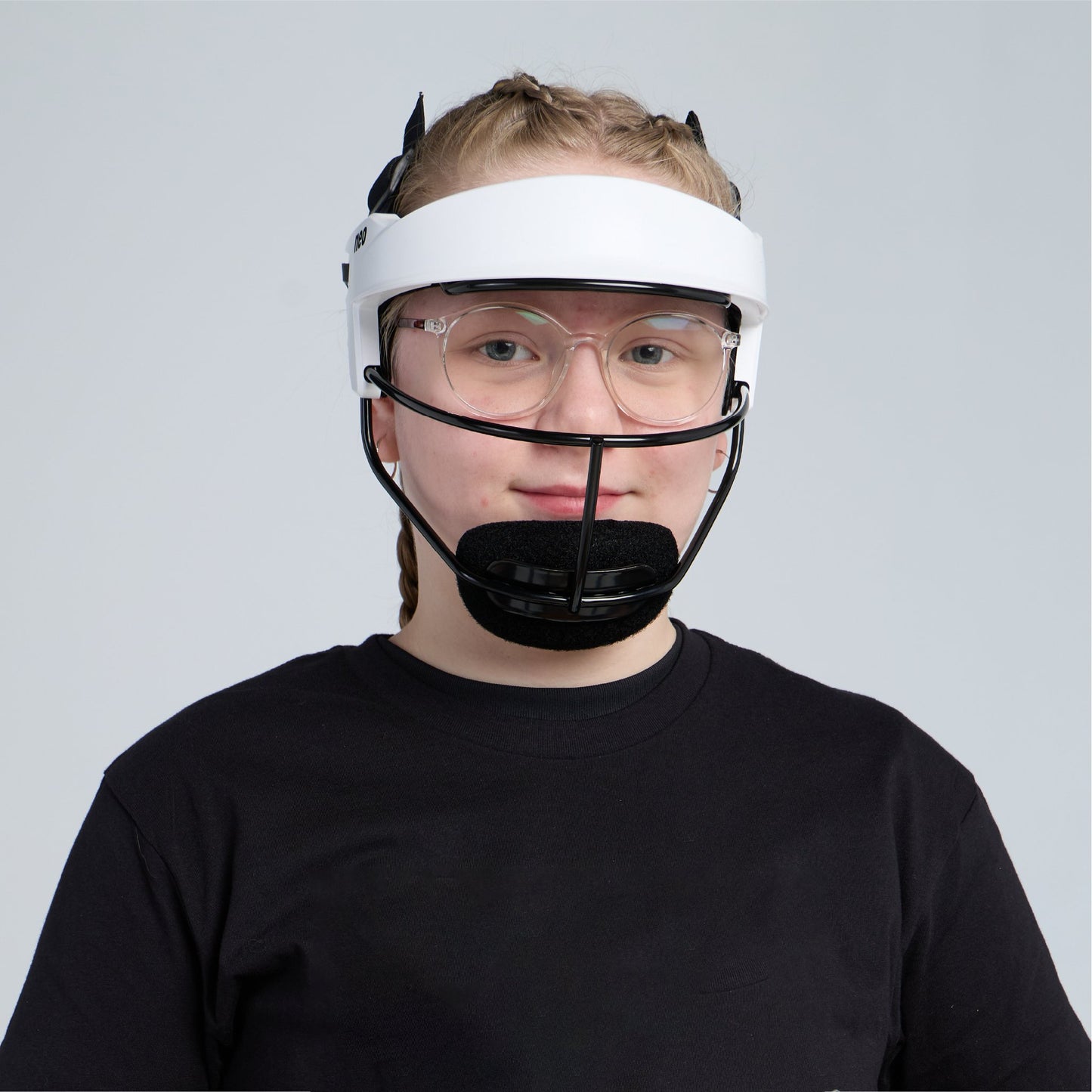 A young softball player with short blond hair and glasses wearing the white fielder's mask and a black T-shirt, facing the camera against a pale gray background.