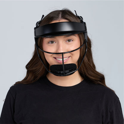 A young softball player with long brown hair wearing the black fielder's mask, facing the camera and smiling, photographed against a pale gray background.