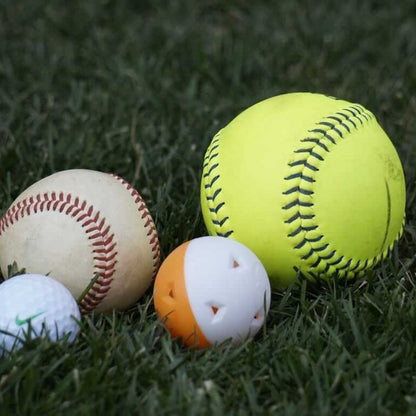 Mini training balls next to a baseball and a softball on grass for size comparison.
