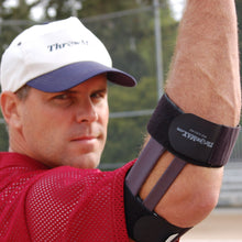 Close-up of a man in a white ThrowMAX cap and red mesh jersey raising his throwing arm, with a black ThrowMAX brace strapped above and below the elbow and dark bars running along the arm.