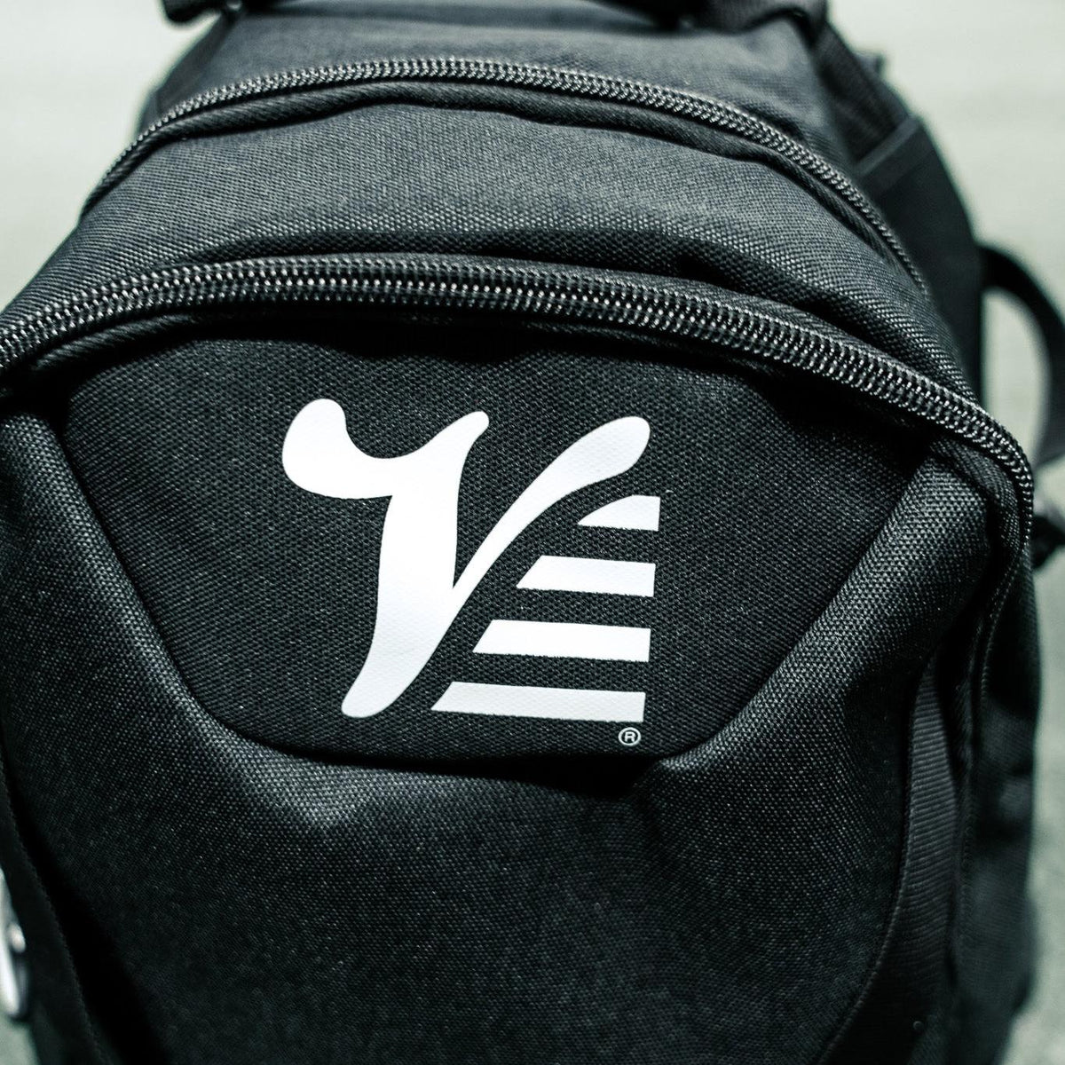 Close up of the white Valle V logo on the top panel of the black baseball backpack