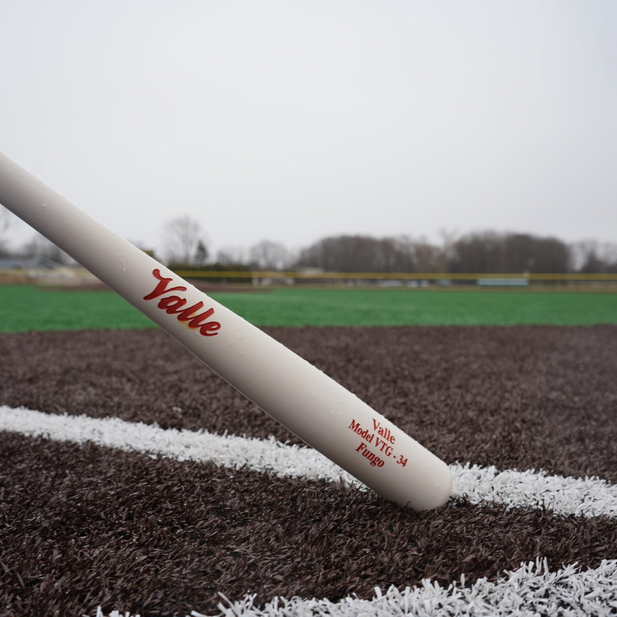 Valle Eagle fungo bat resting on the foul line of a turf field, the barrel stamp reading Model VTG 34 Fungo