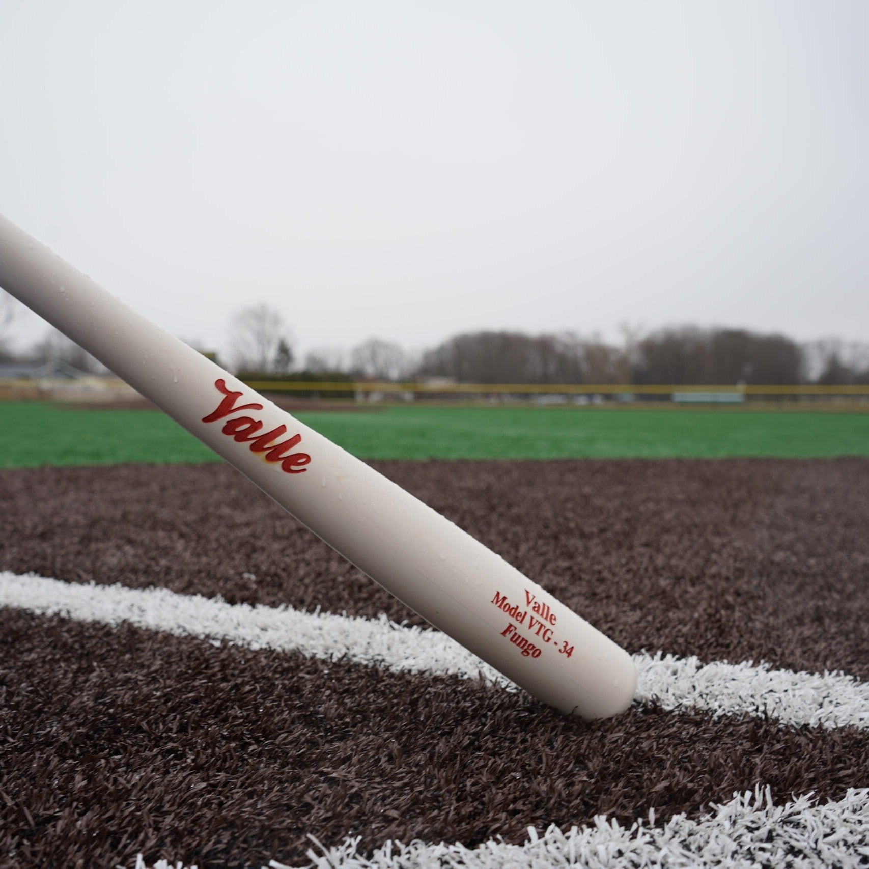 Valle Eagle fungo bat resting on the foul line of a turf field, the barrel stamp reading Model VTG 34 Fungo