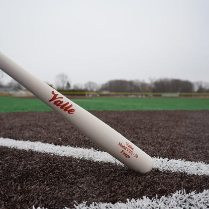 Valle Eagle fungo bat resting on the foul line of a turf field, the barrel stamp reading Model VTG 34 Fungo