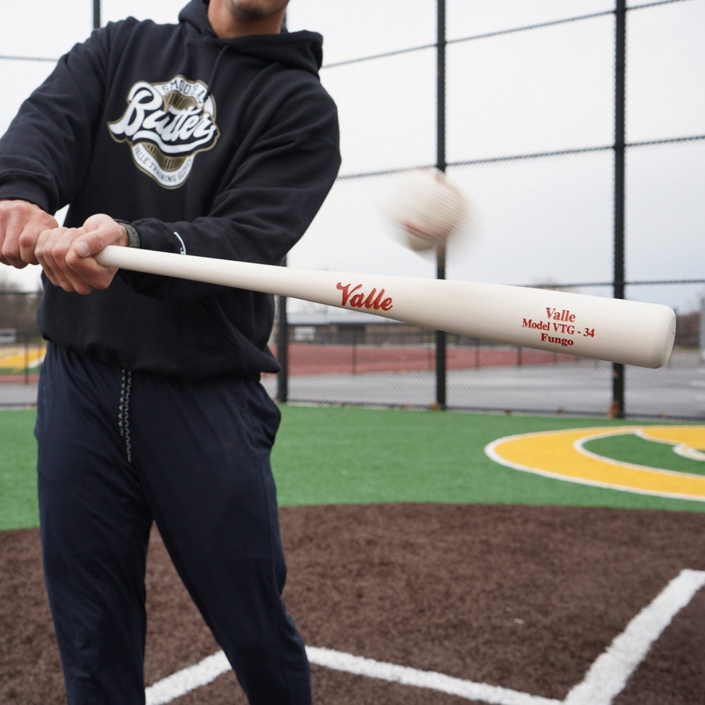Coach hitting a fungo on a turf infield with the baseball just off the barrel