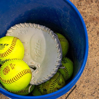 Valle Eagle KK four-finger training glove, the glove resting in a bucket of yellow softballs