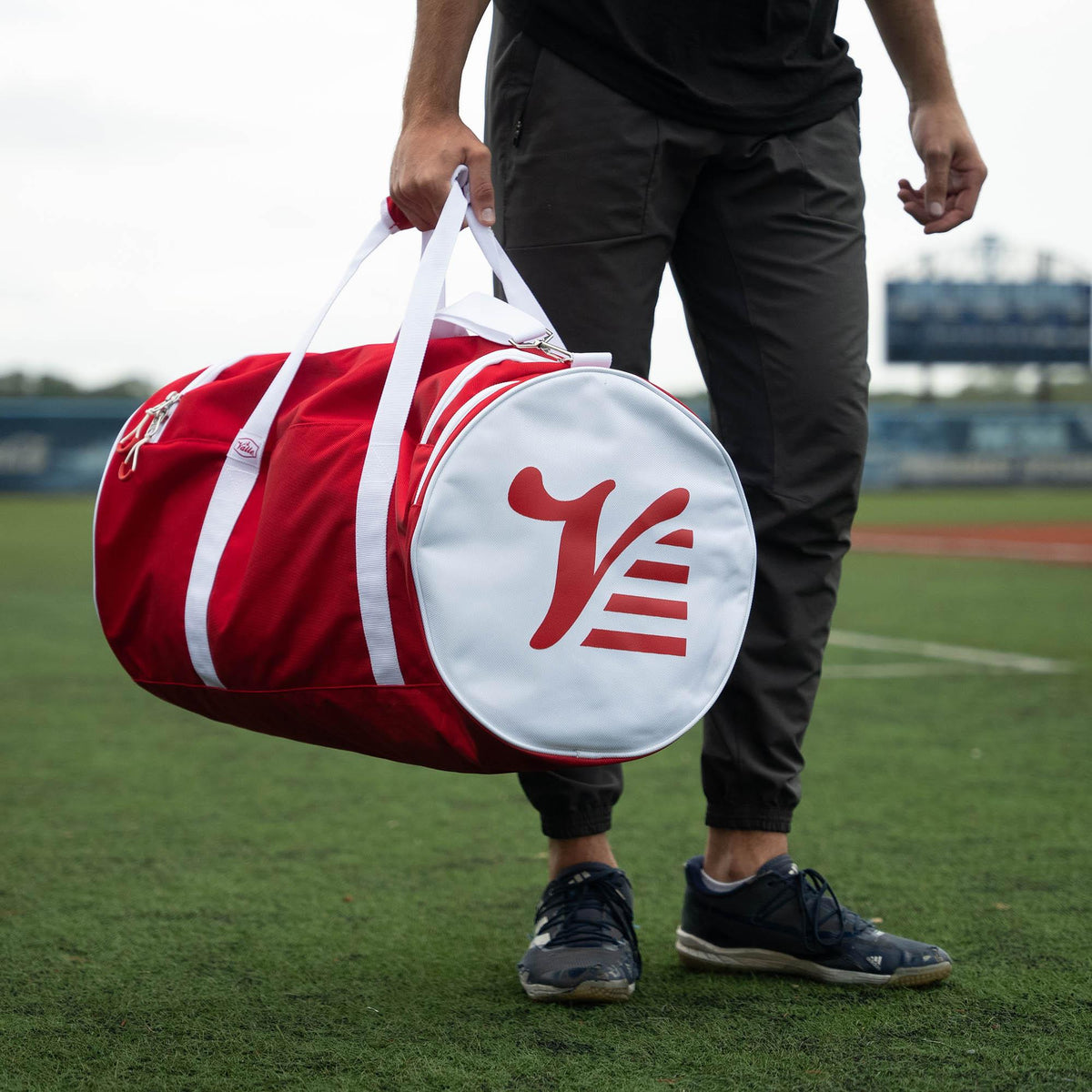 Red Valle Eagle Players Duffle Bag carried by its top handles at the field, white logo end cap facing out