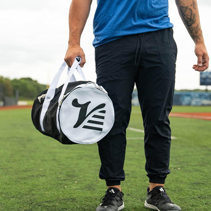 Player carrying the black Valle Eagle Youth Equipment Bag by its handles at the field, logo end cap out